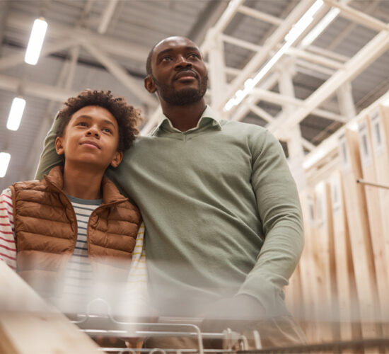 Low angle portrait of African-American father and son shopping together in hardware store while pushing cart with wooden boards for construction or home improvement